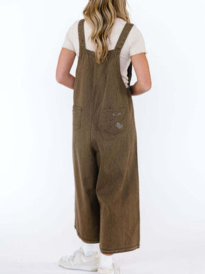 Brown relaxed fit denim overalls with distressed pockets and wide legs.