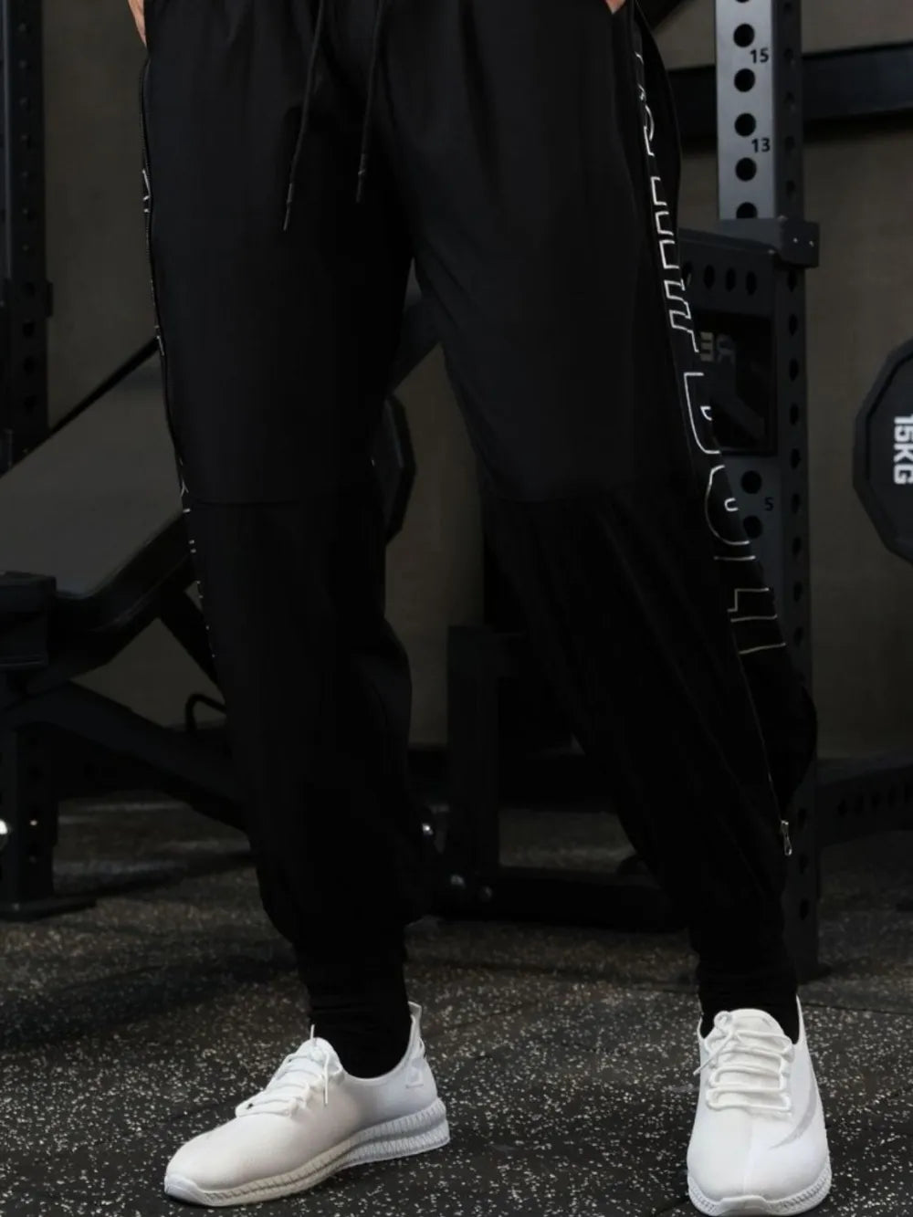 Black track pants with zip detail and white side graphic, worn with white sneakers.