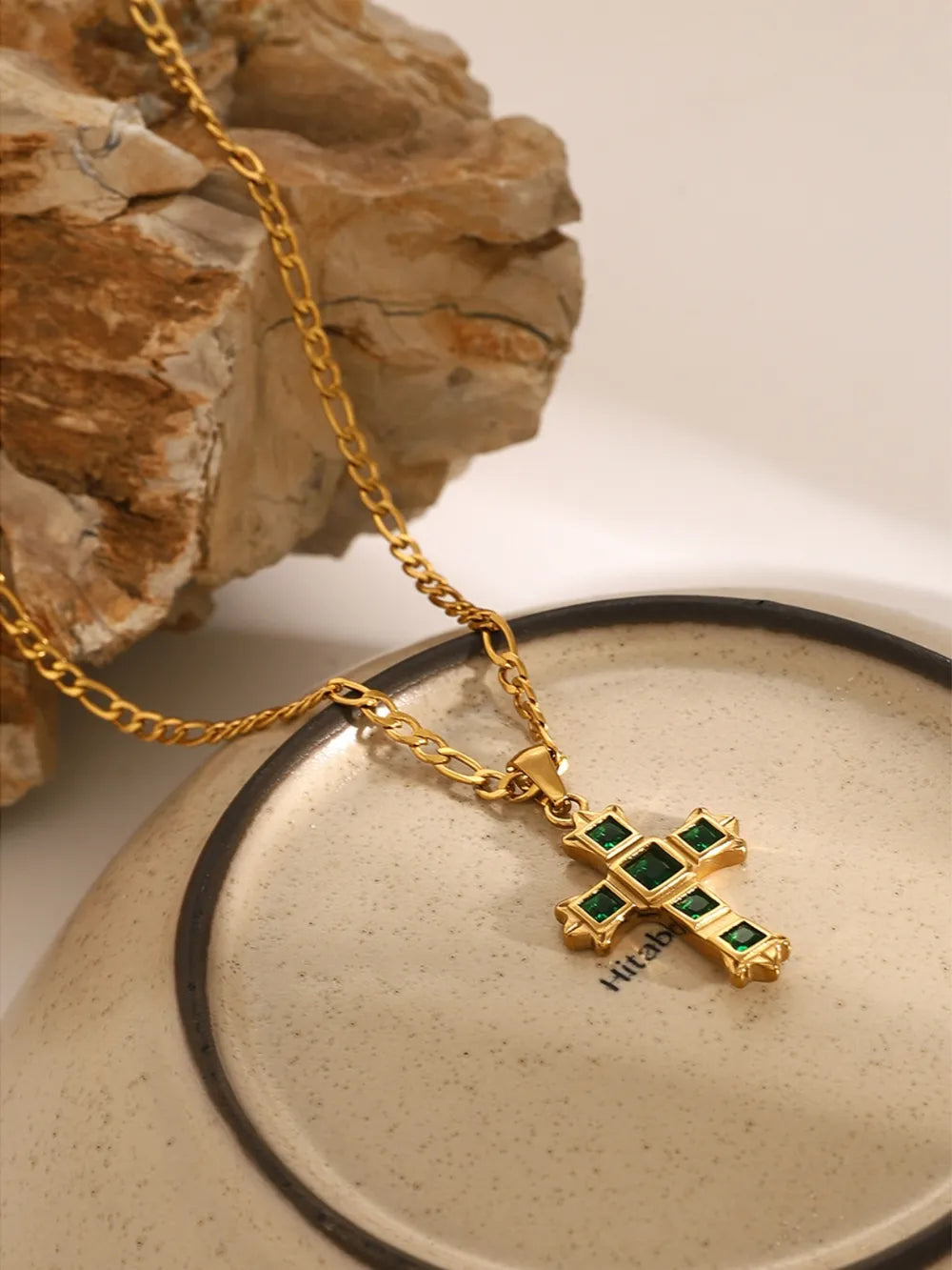 Gold cross pendant necklace with green zirconia stones on a figaro chain.