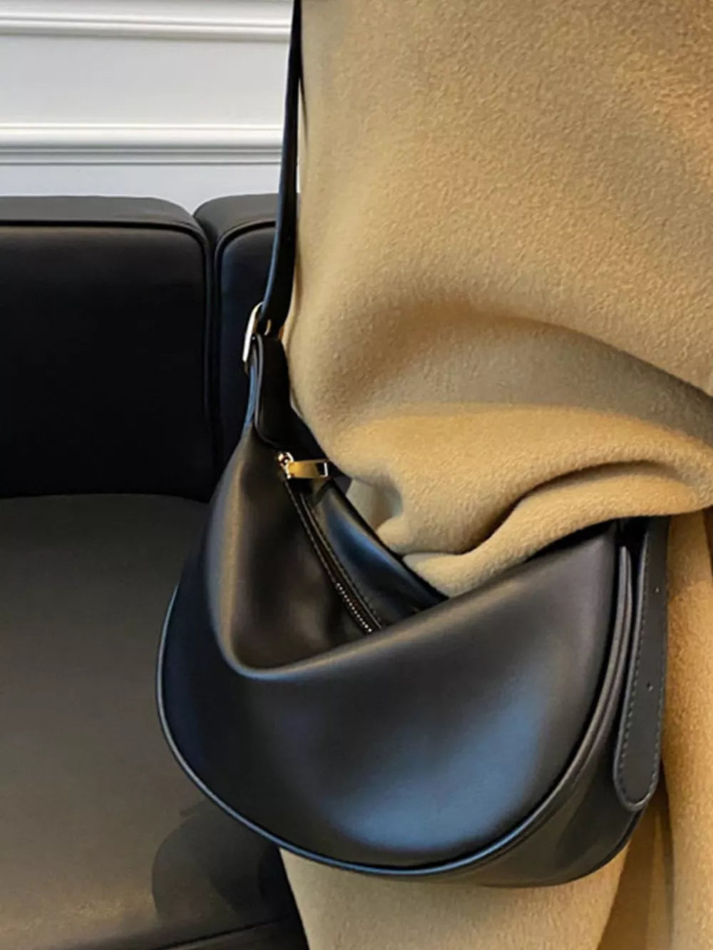 Black crescent crossbody bag with adjustable strap and zipper detail.