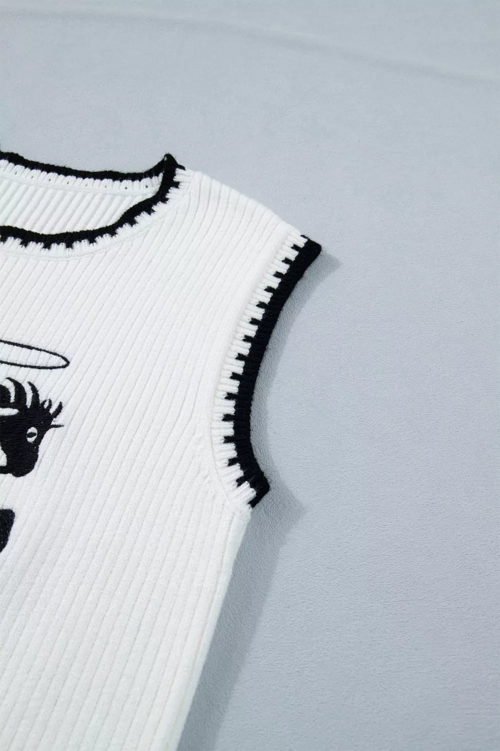 White knit sweater vest with black contrast trim and rodeo graphic detail.