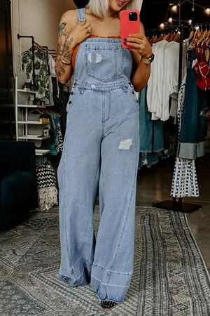 Distressed light wash denim wide-leg overalls with a bib pocket and button details.