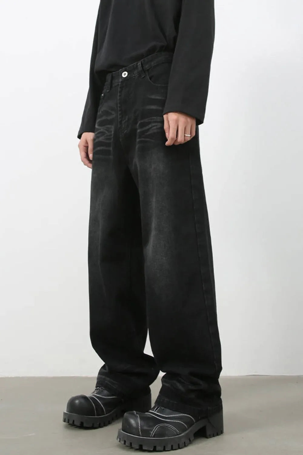 Faded black baggy denim trousers with a relaxed fit, styled with chunky boots.