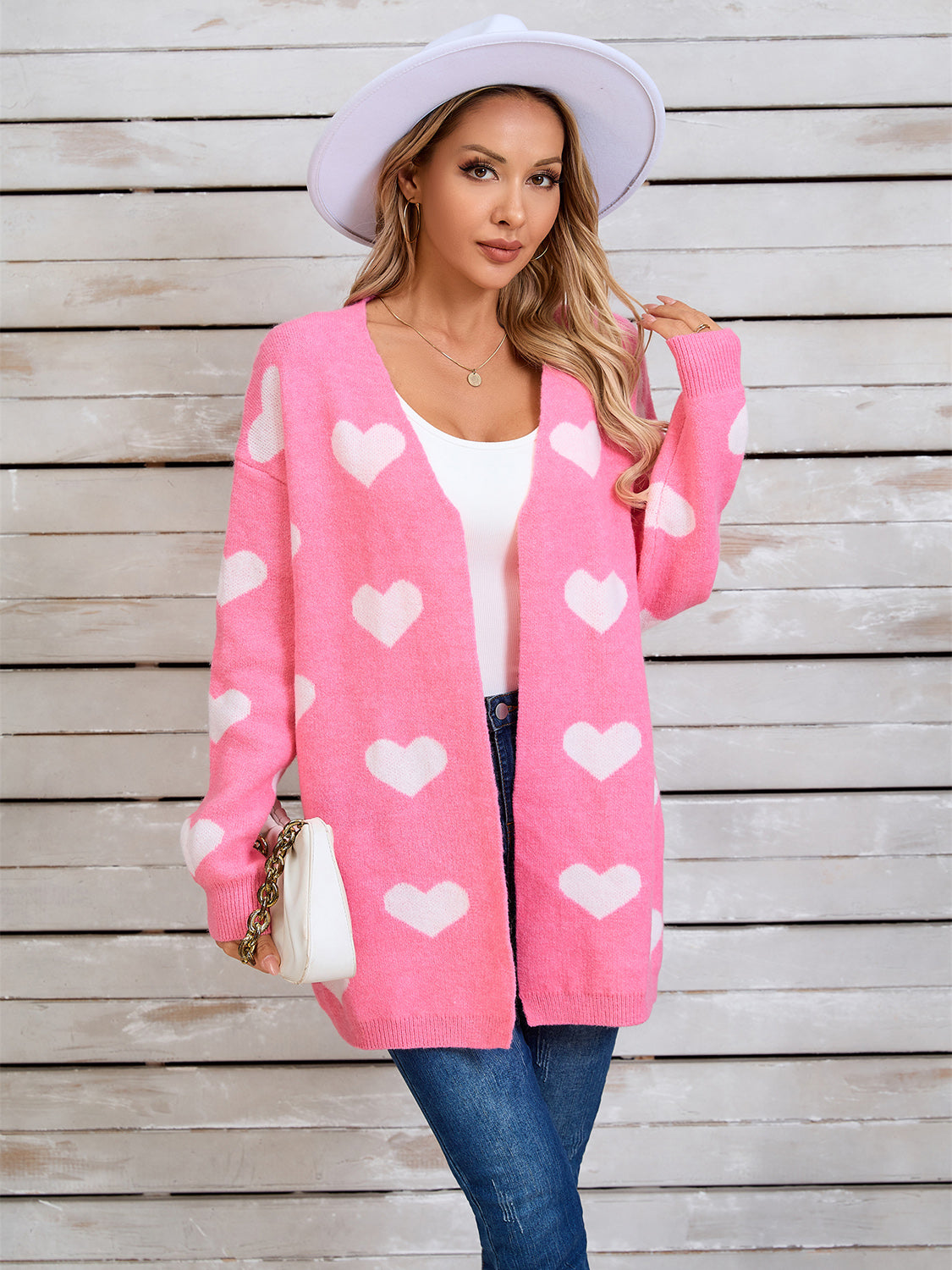 Pink acrylic cardigan with white heart intarsia pattern, open front, long sleeves.