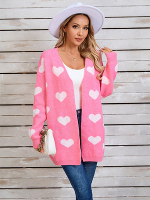 Pink acrylic cardigan with white heart intarsia pattern, open front, long sleeves.