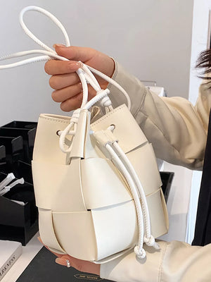 Chic woven white mini bucket bag with drawstring closure and tassel detail.