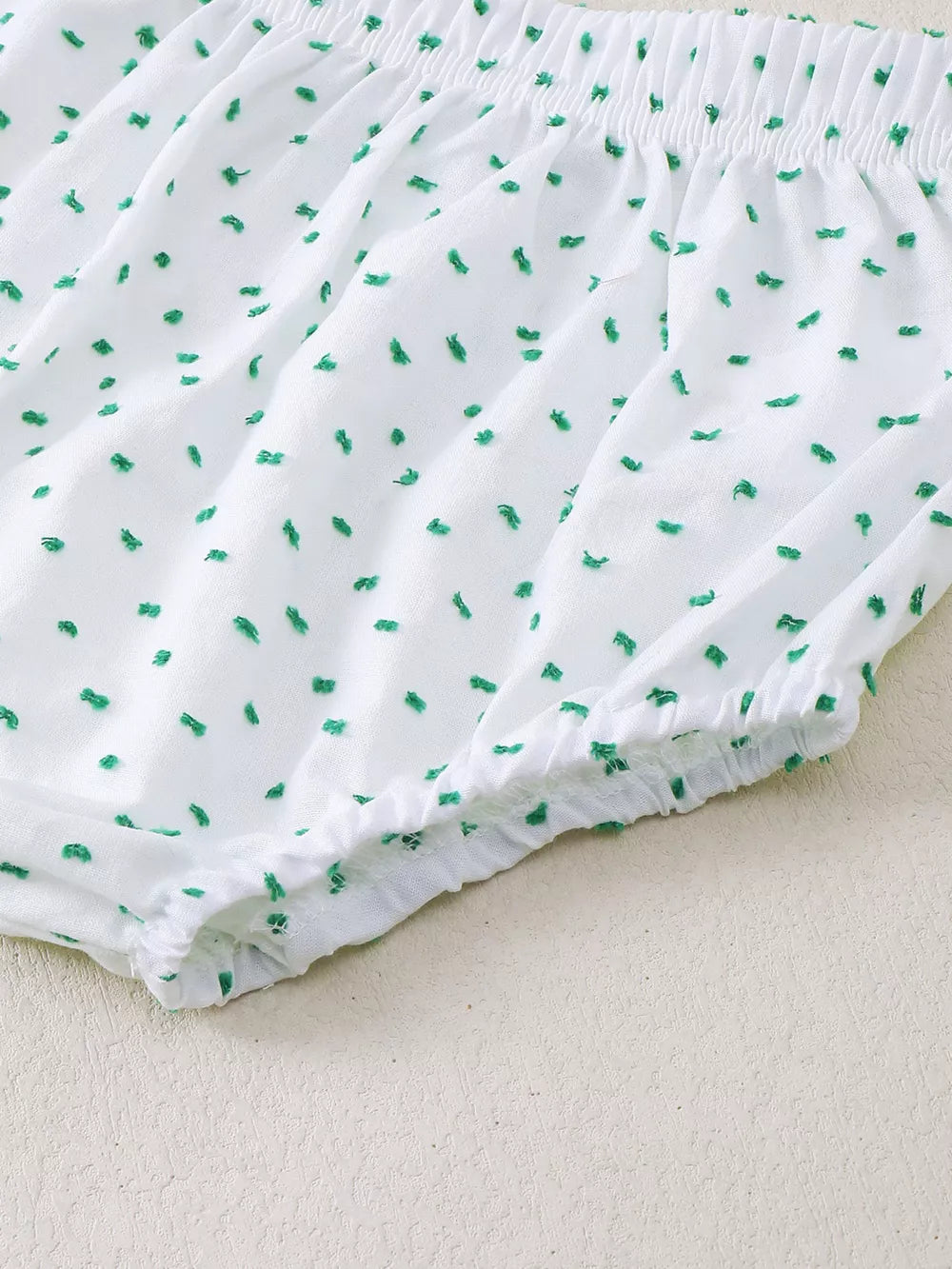 White baby shorts with green dobby dots and elastic waistband and leg openings.
