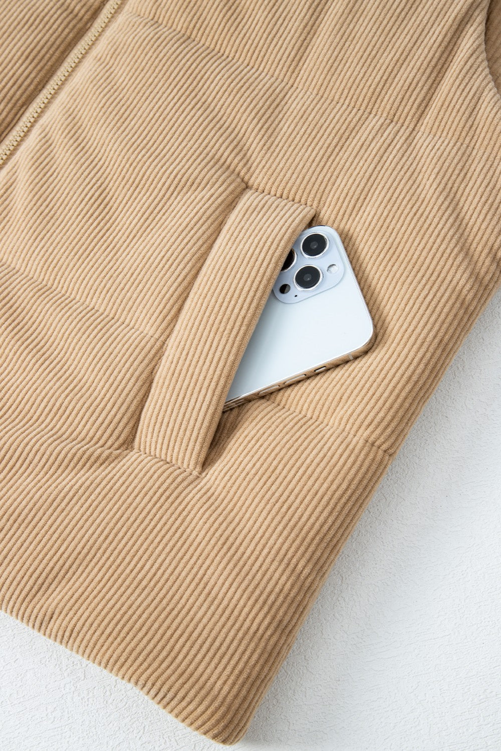 Tan corduroy padded funnel neck vest with a phone in the pocket.
