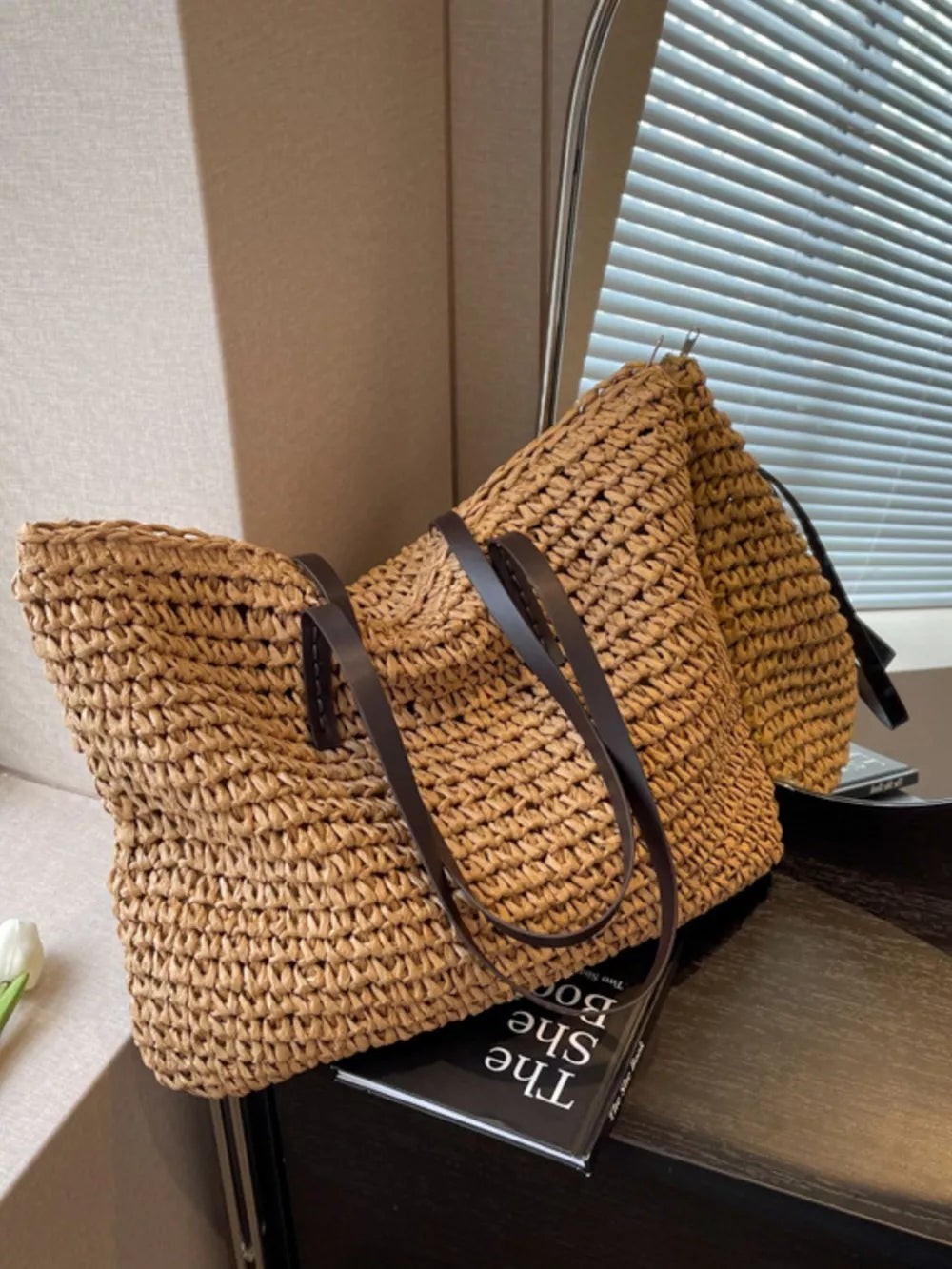 Natural woven straw shoulder bag with dark brown leather straps.