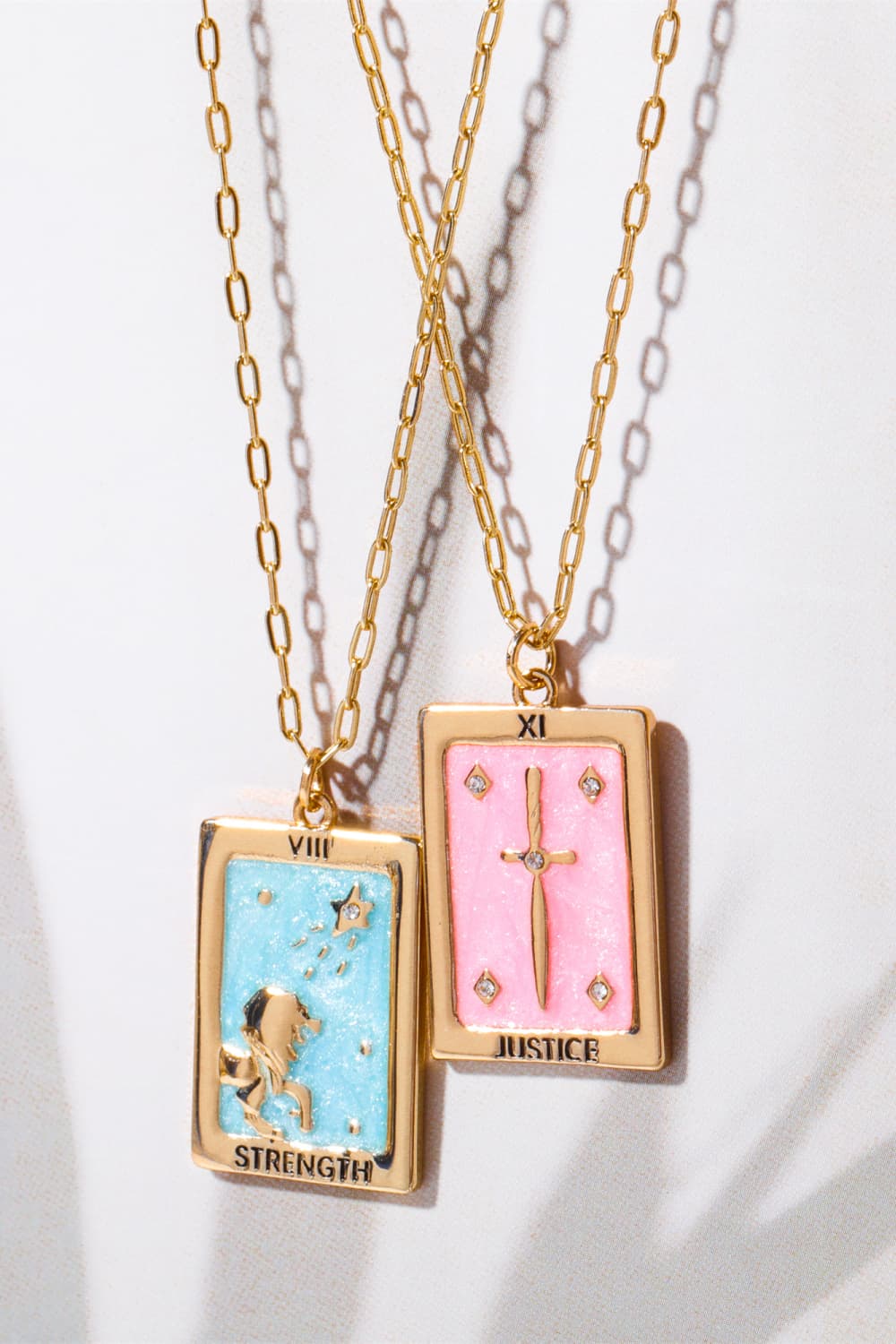 Tarot card pendant necklaces in light blue and blush pink with gold chains and charms.