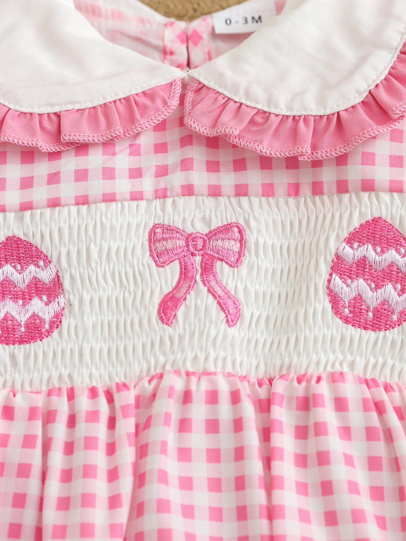 Pink gingham baby one-piece with smocking, embroidered bow, and Easter eggs.