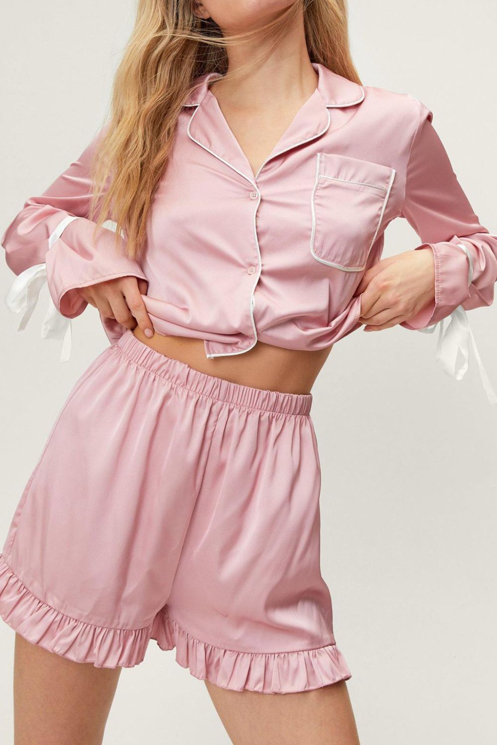 Blush pink silk pajama set with white trim, bow tie sleeves, and ruffled shorts.