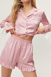 Blush pink silk pajama set with white trim, bow tie sleeves, and ruffled shorts.