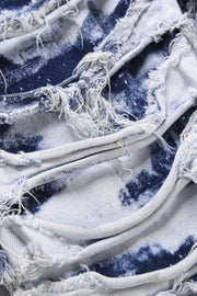 Distressed shredded denim jeans in medium wash with artistic blue tie-dye pattern and frayed edges.