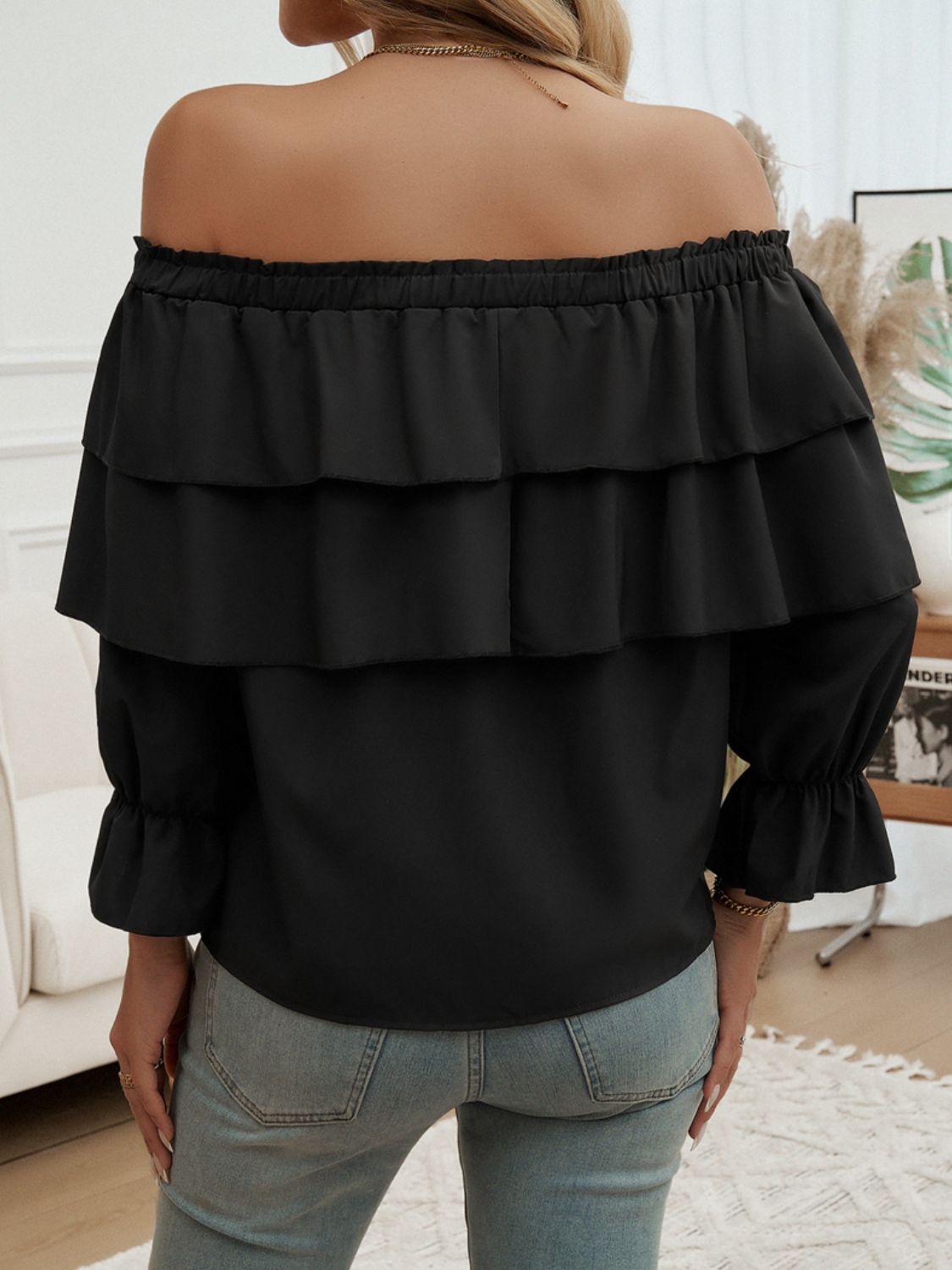 Black tiered ruffle off-shoulder blouse with long sleeves and ruffled cuffs.