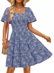 Smocked mini dress in dusty blue with tiered skirt and floral pattern. Square neck, flutter sleeves.