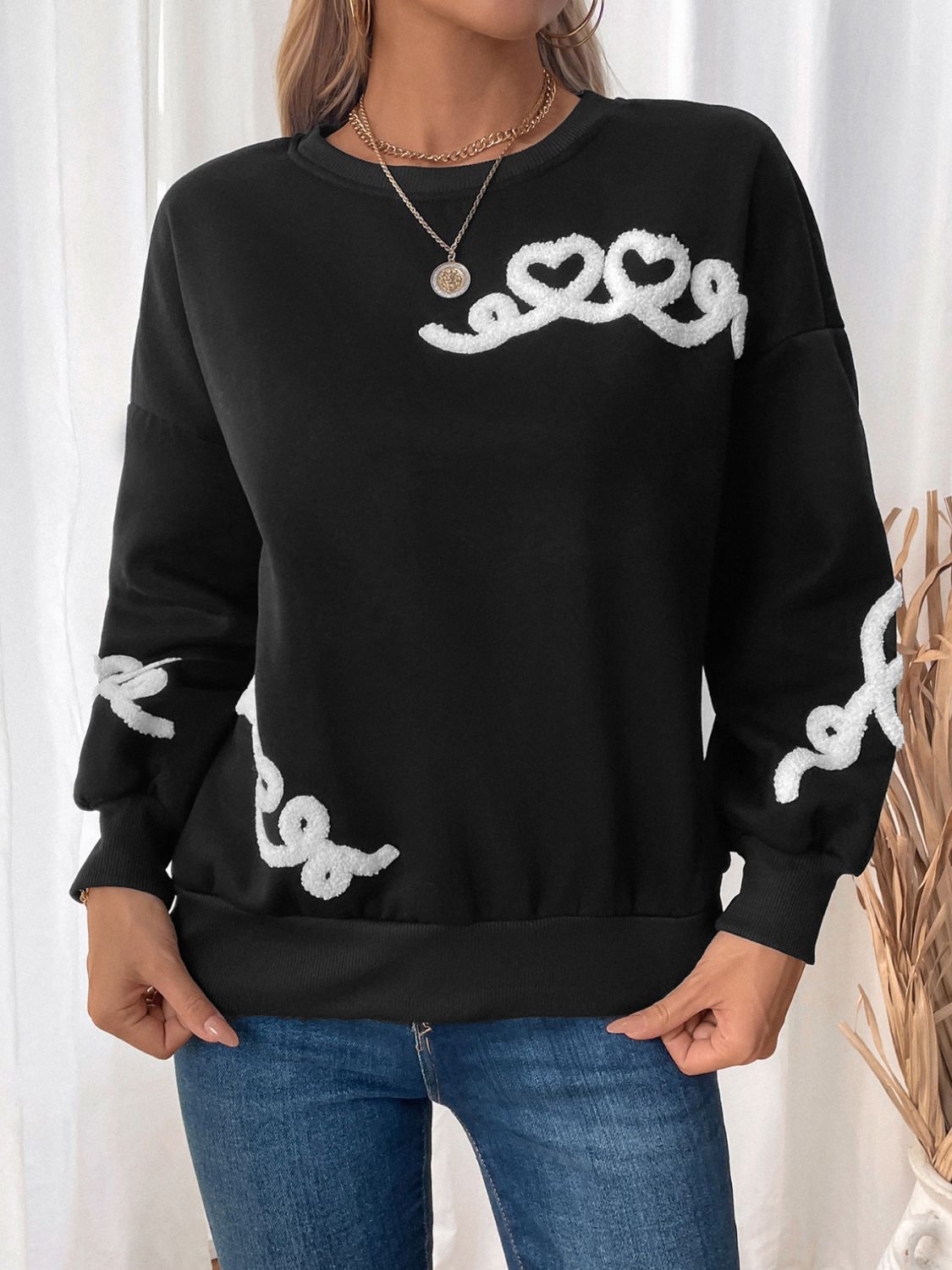 Black crewneck sweatshirt with embroidered white heart detail on sleeve and chest.