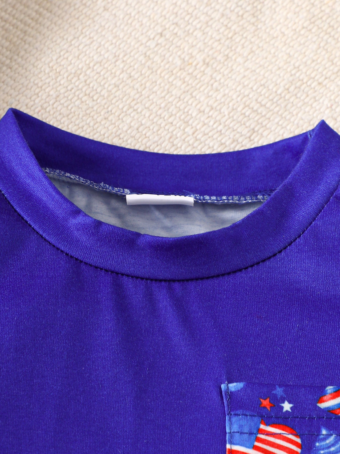 Baby tee with American flag pocket detail, round neck, short sleeves.
