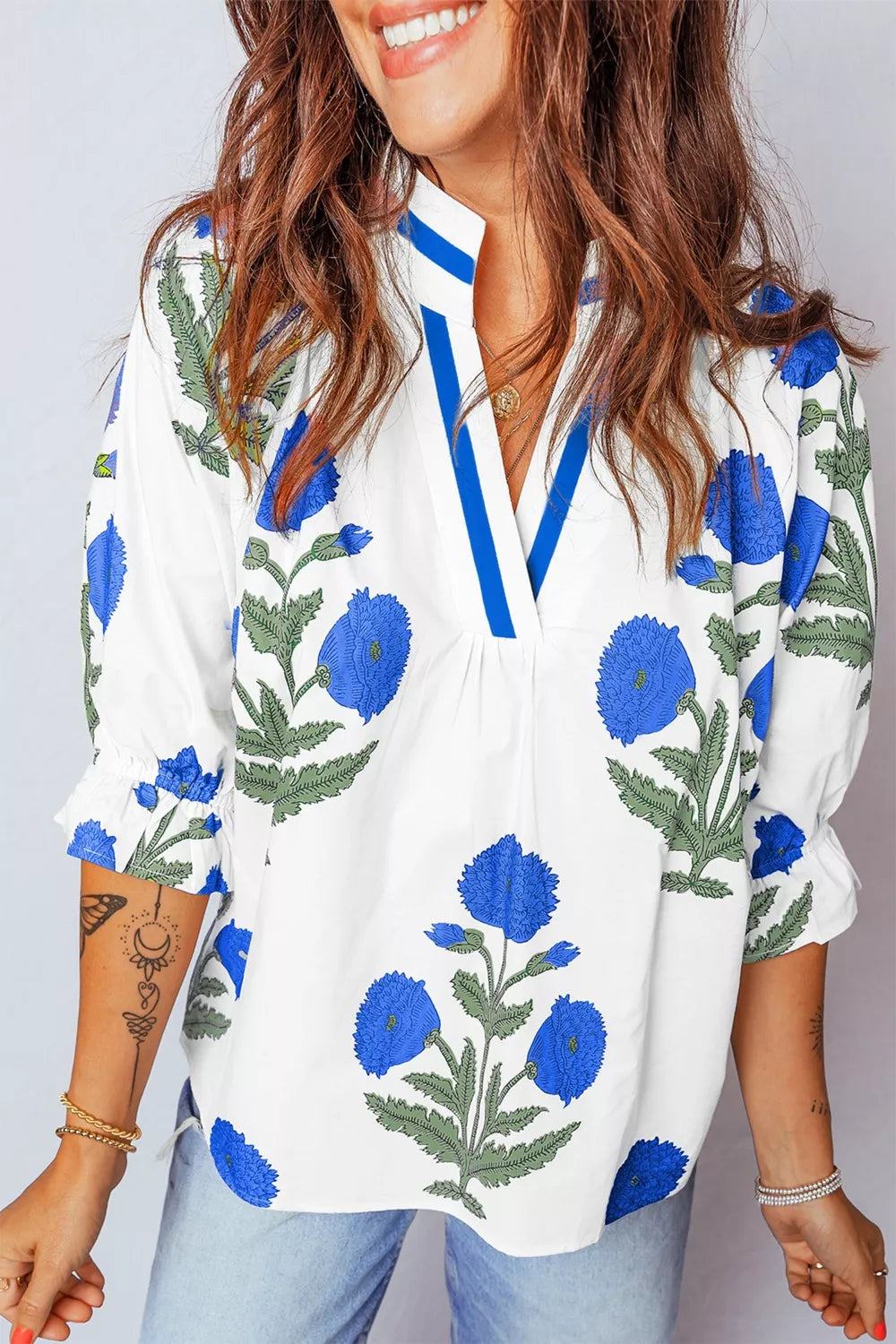 White cotton blouse with blue floral print, notched neckline, and ruffled sleeves.
