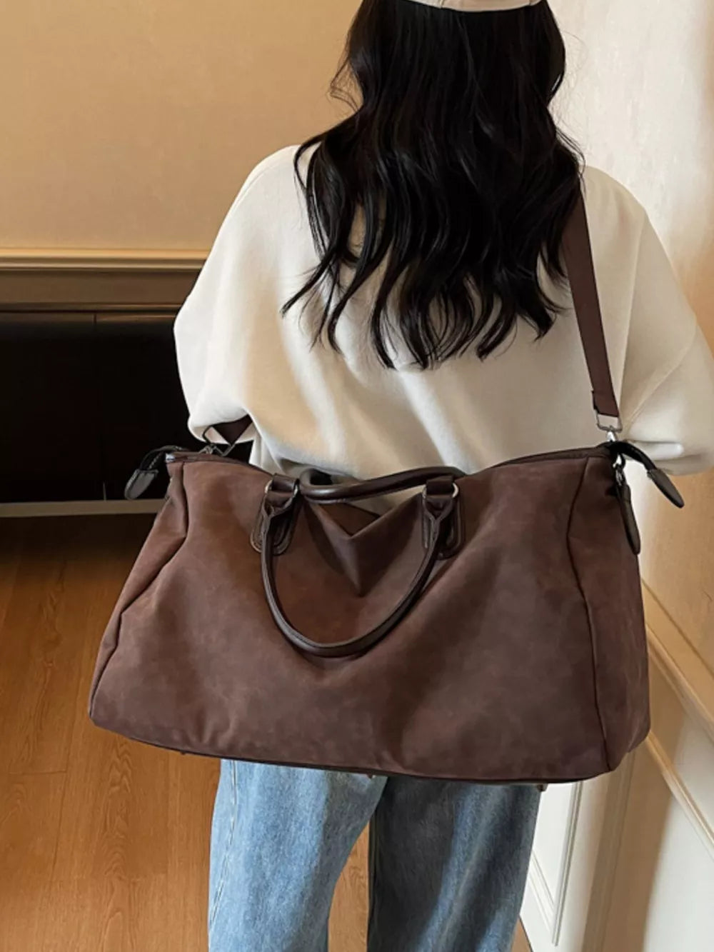 Chocolate brown duffel bag with adjustable strap and twin handles, worn by a woman.