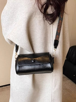 Black leather mini crossbody bag with a decorative ethnic strap and button closure.