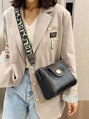Black crocodile pattern mini crossbody bag with decorative strap and gold button closure.