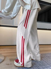 Men's light gray wide-leg sweatpants with bold red stripes on the sides.
