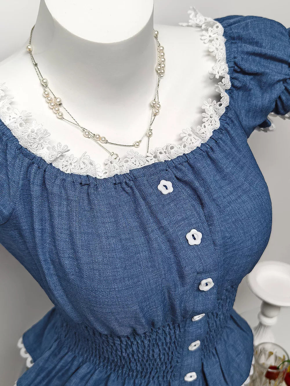Blue denim maternity blouse with puff sleeves, lace trim, and decorative flower buttons.