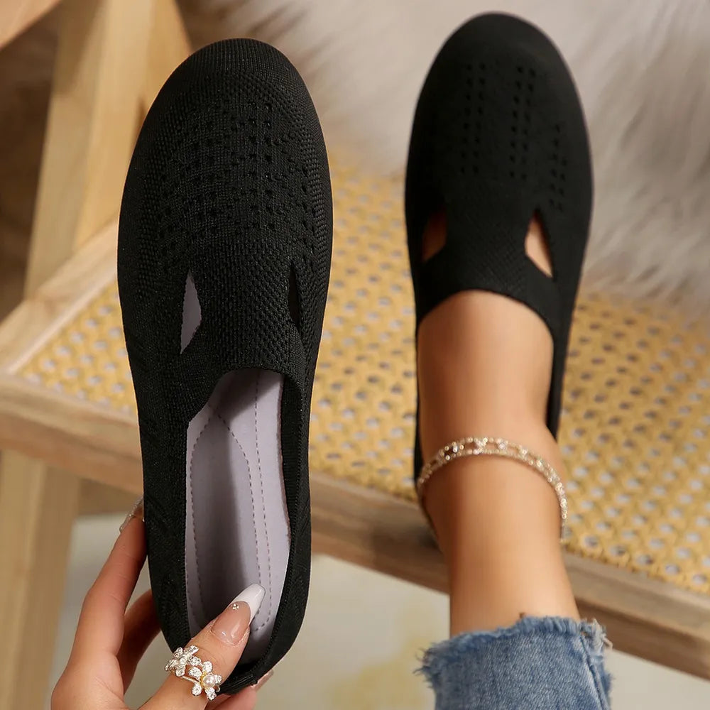 Black knit slip-on flats with cutout details and perforated pattern.
