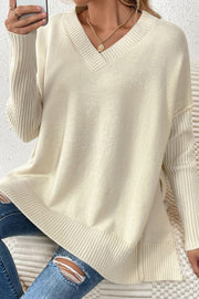 Cream v-neck knit sweater with ribbed sleeves and asymmetric hemline, styled with jeans.