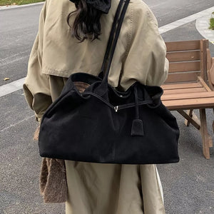 Black suede slouchy shoulder bag with drawstring detail and leather tag.