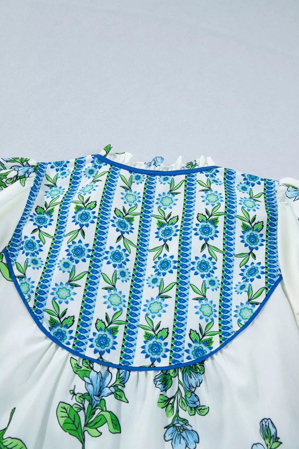 White polyester shirt with blue floral print and striped bib detail.