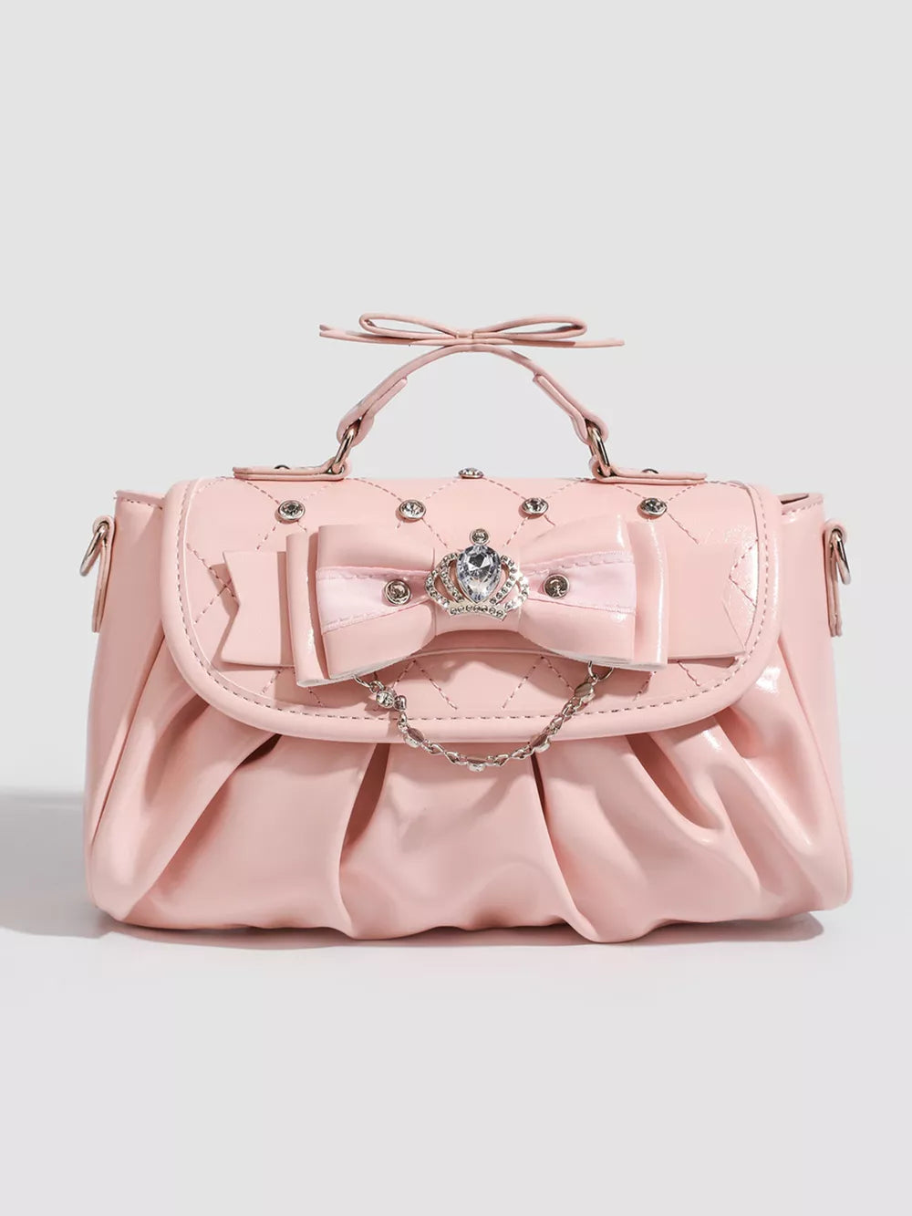 Pink ruched crossbody bag with bow, crown charm, and chain detail.