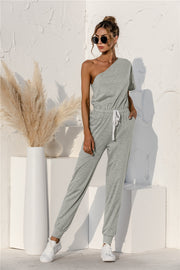 Gray asymmetric sweat jumpsuit with drawstring waist and cuffed jogger legs.