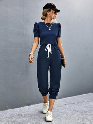 Dark blue jumpsuit with puffed short sleeves, drawstring waist, and cuffed ankles.