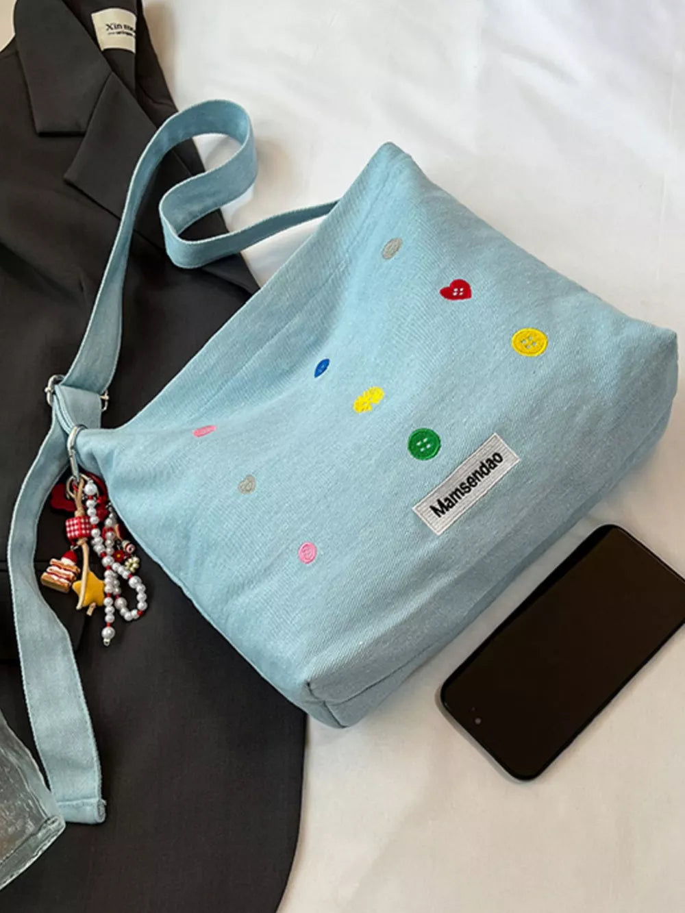 Light blue denim crossbody bag with colorful button embroidery and adjustable strap.