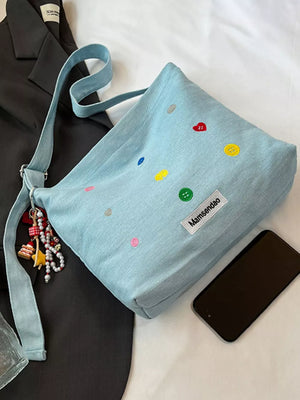 Light blue denim crossbody bag with colorful button embroidery and adjustable strap.