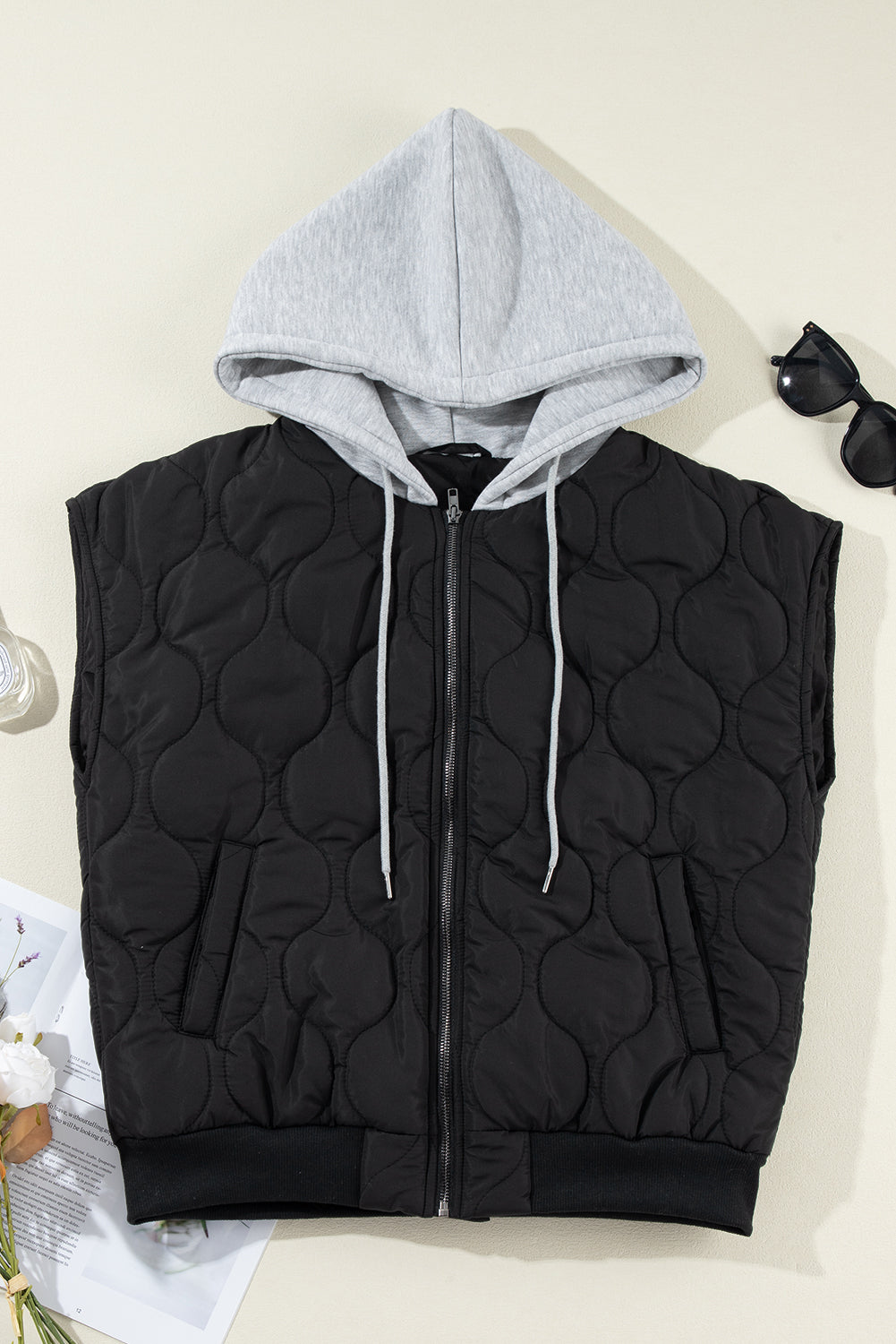 Black quilted sleeveless jacket with grey hooded neckline and white drawstrings.