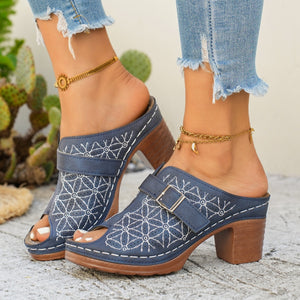 Blue leather sandals with white floral cutouts and buckle detail on block heel.