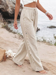 Relaxed beige wide-leg trousers with drawstring and shell trim detail.