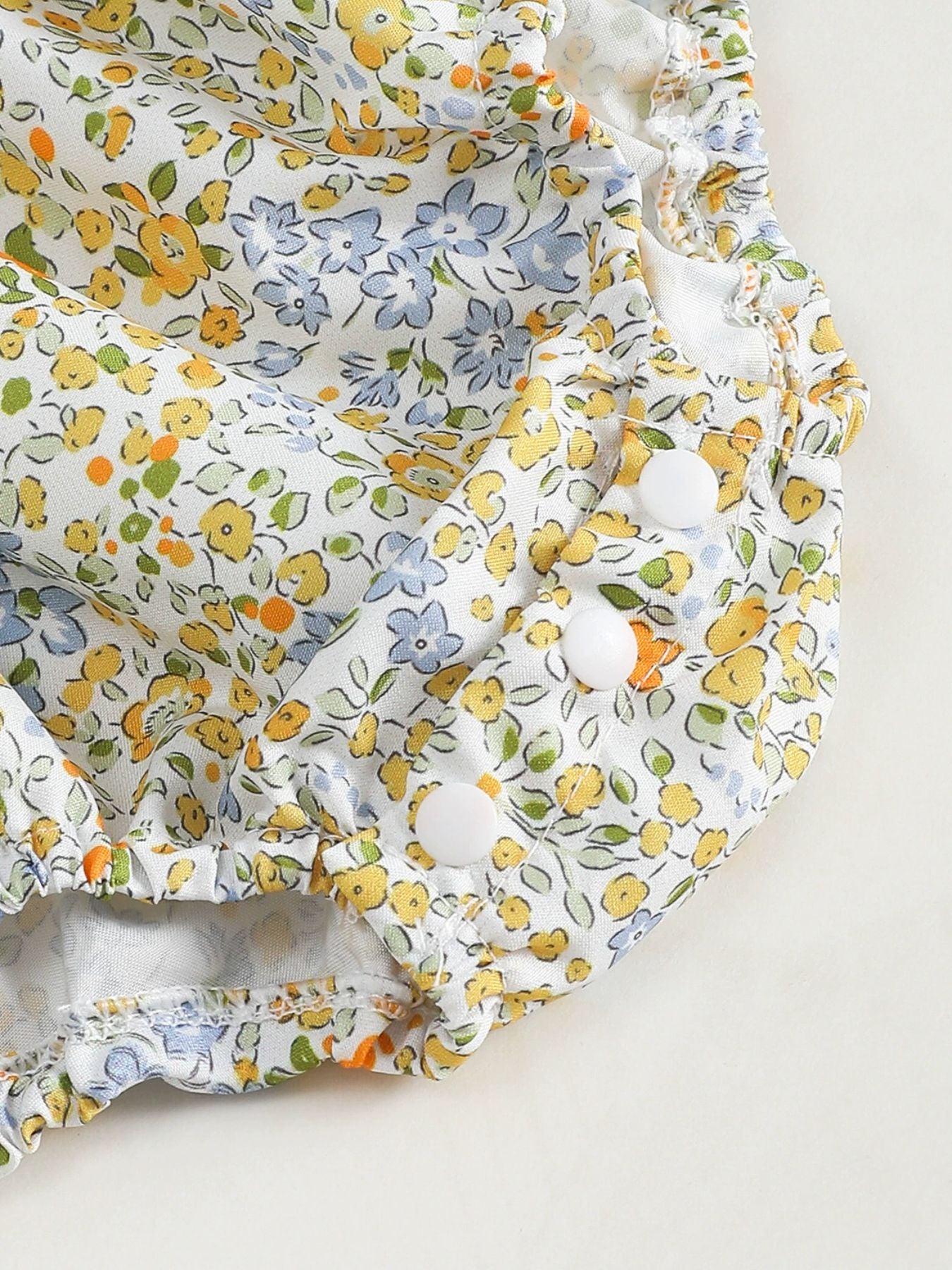 Baby one-piece with white floral print, yellow, blue, and orange flowers, and white buttons.