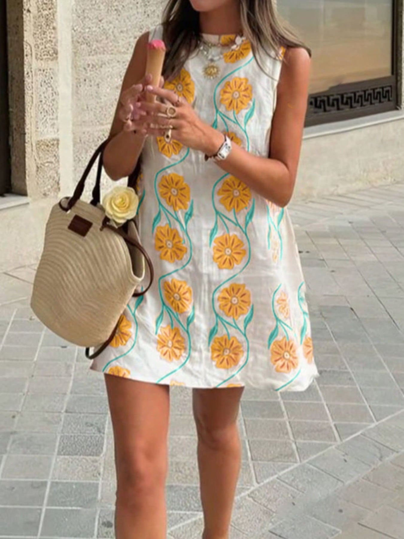 Delicate floral mini dress with high neckline in white with yellow flowers and green stems, sleeveless, above knee length.
