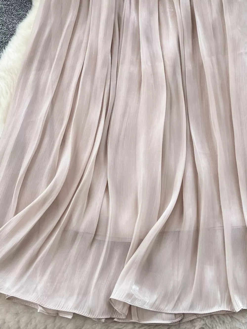 Cream pleated maxi skirt with flowing fabric and subtle sheen.