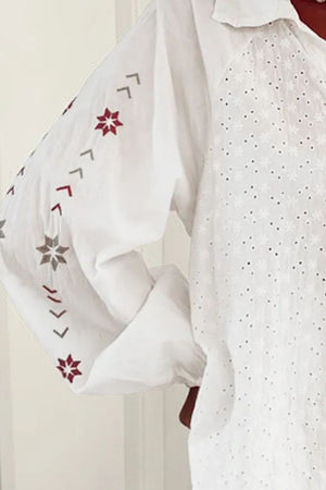 White eyelet blouse with blouson sleeves featuring embroidered geometric and star patterns.