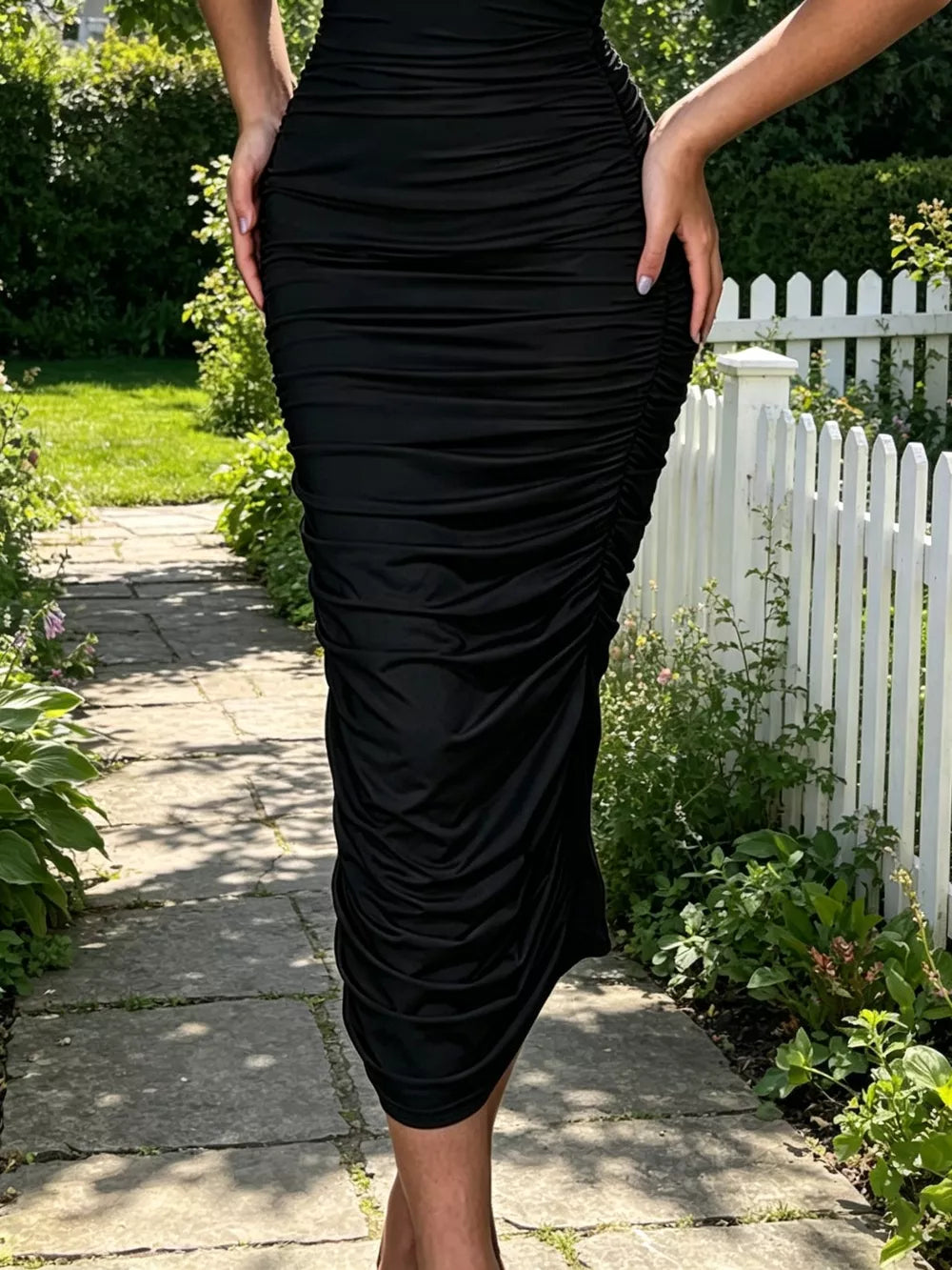 Black ruched bodycon midi dress with floral appliqué detail.