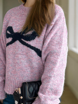 Pink intarsia knit sweater with black bow detail, crew neck, long sleeves, acrylic blend.