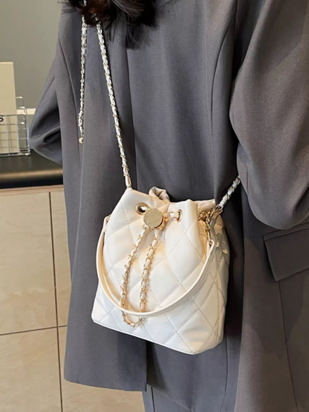 Chic quilted bucket crossbody bag in white with gold chain detail.
