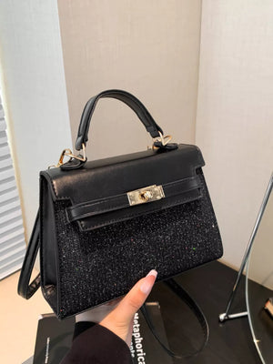 Black glitter textured mini crossbody bag with gold hardware and top handle.