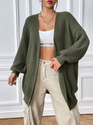 Olive green ribbed knit cardigan with balloon sleeves and an open front, styled with a white crop top and beige pants.