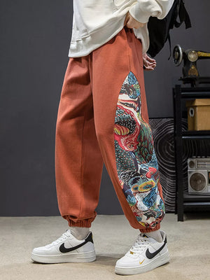 Men's orange joggers with vibrant side panel print and elastic cuffs.
